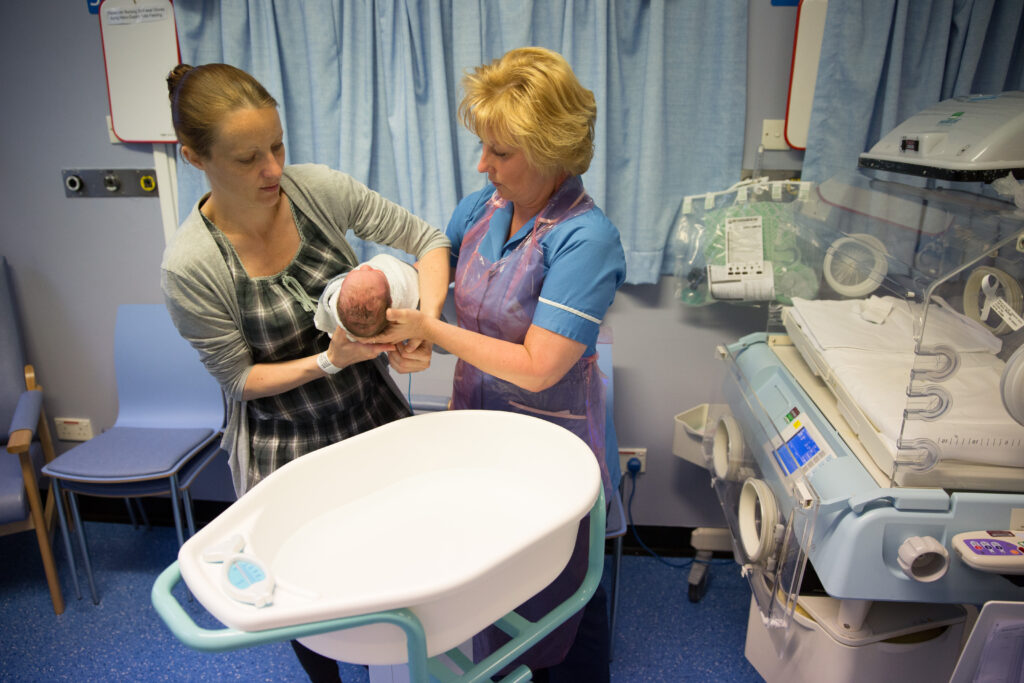 Photograph of a parent taking their baby from a nurse