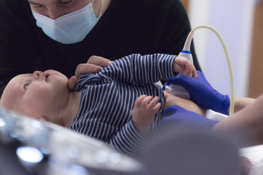 The photograph shows a baby having a hip scan