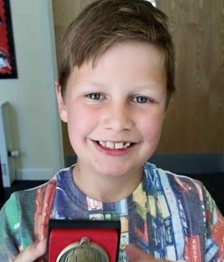 Young boy in a multi coloured top holding a medal.