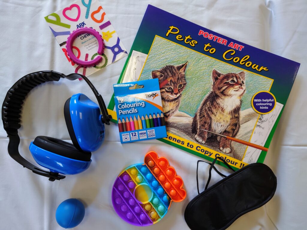 A selection of distraction aids and sensory items, including a pair of ear defenders, a colouring book and pencils, and a stress ball.