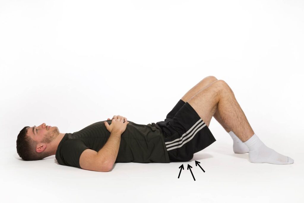 Photograph of a person lying on the floor with their knees raised squeezing their buttock muscles.