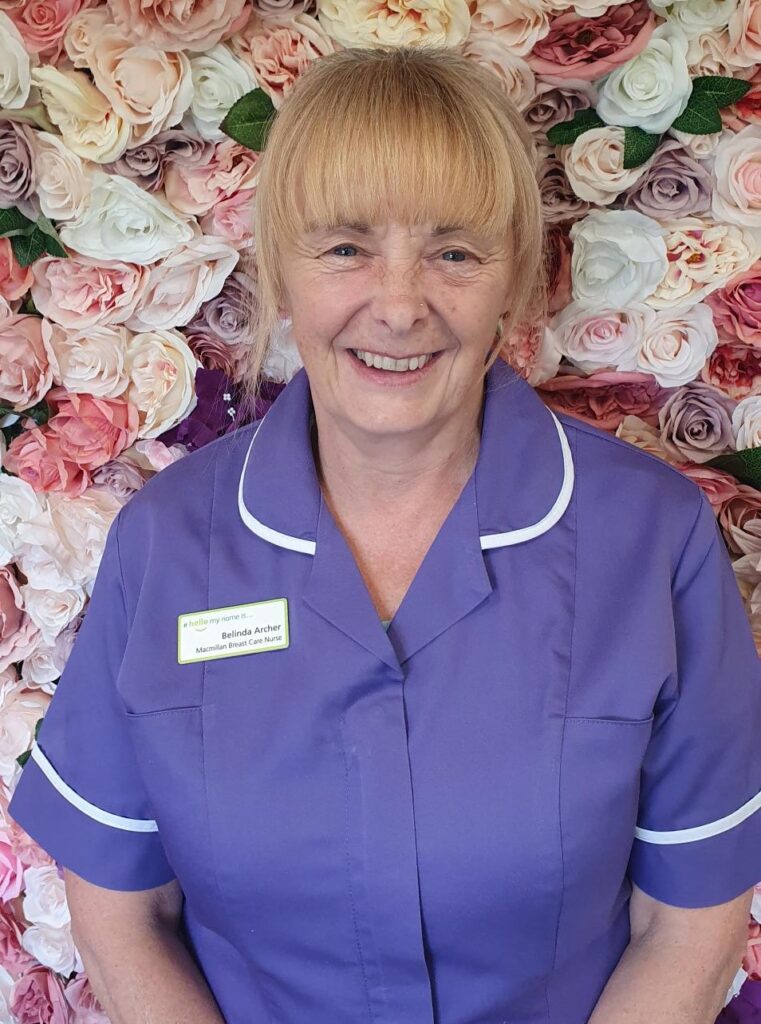 Photo of Belinda dressed in purple nurses uniform with flower background 