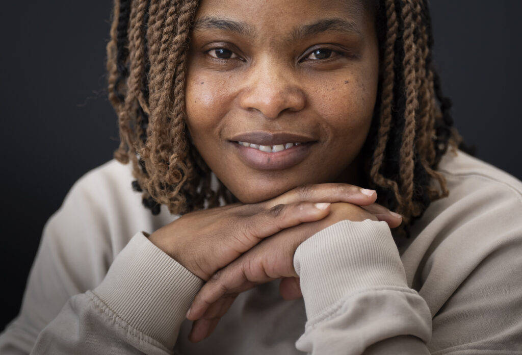 An image of the patient Ruvimbo smiling to camera with her hands under her chin.