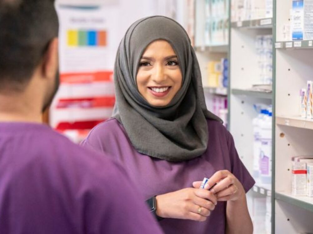 Two people standing in front of a pharmacy dispensary.